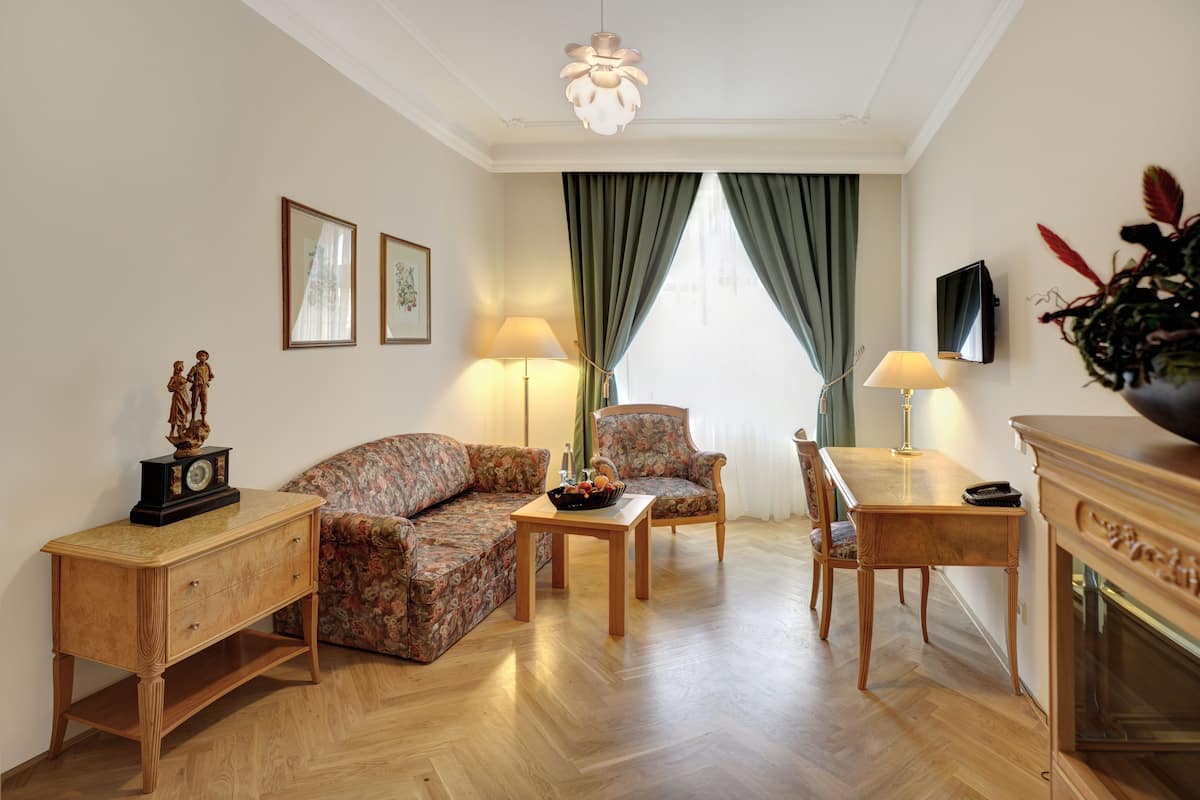 Een woonkamer met een bank, fauteuil, houten salontafel en een bijzettafeltje met een klok.