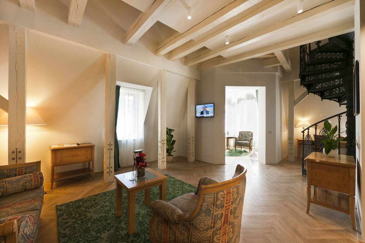 Een ruime woonkamer met houten balken, een bank, een stoel, een tafel en een trap.