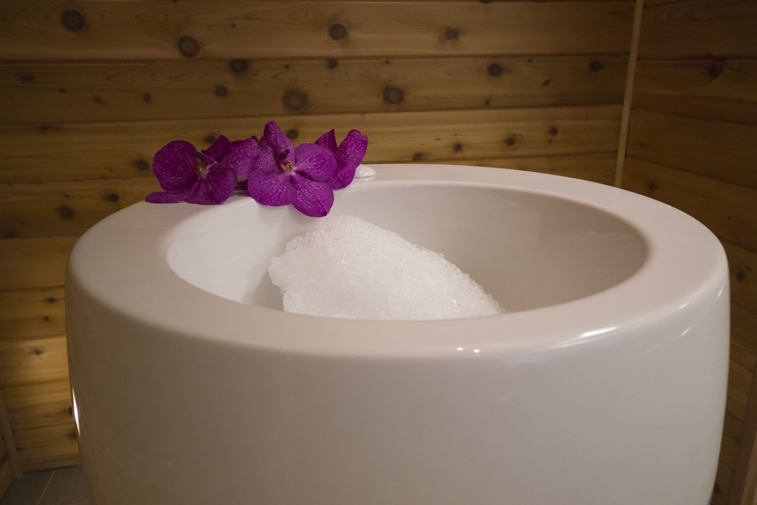 A white bathtub with a purple orchid in a wooden cabin setting.