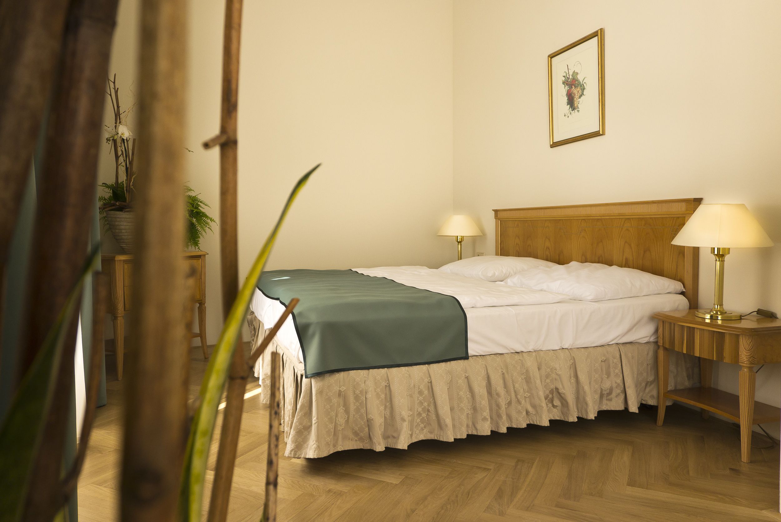 A neatly made bed with a wooden headboard, two bedside lamps, and a framed picture on the wall.