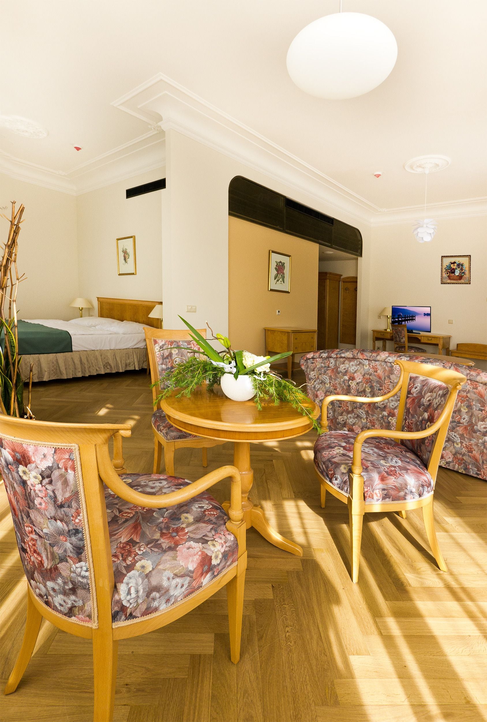 A hotel room with a bed, a dining table with chairs, a sofa, and a TV.