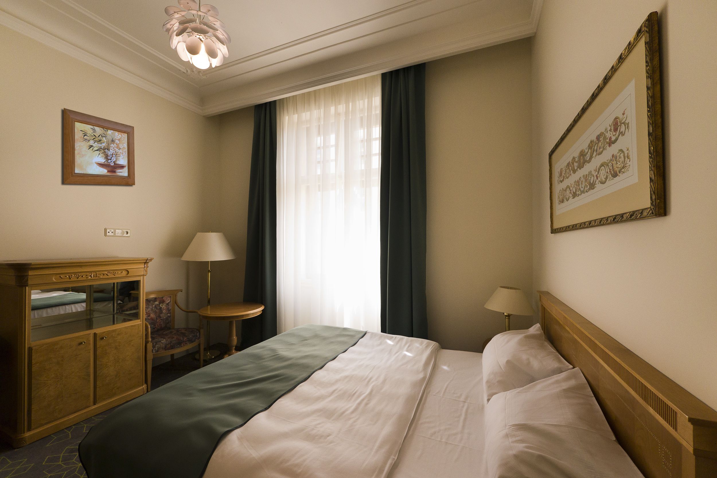 A hotel room with a bed, a desk, a chair, a lamp, and a framed picture on the wall.