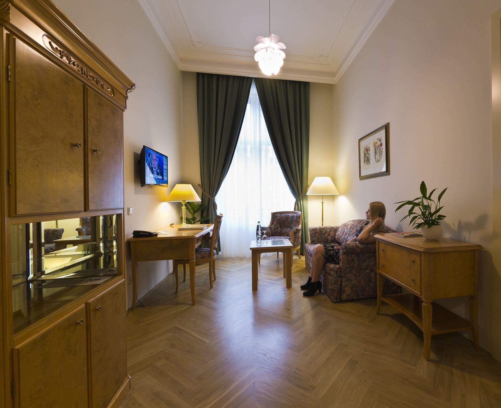 Ett hotellrum med trägolv, en soffa, ett skrivbord med en lampa, en tv och ett skåp.