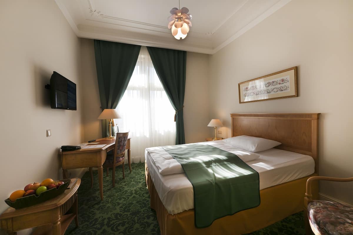Een hotelkamer met een bed, bureau, stoel en een televisie aan de muur.