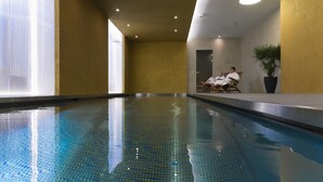Una piscina interior con agua azul cristalina, una pared amarilla y una planta en maceta.