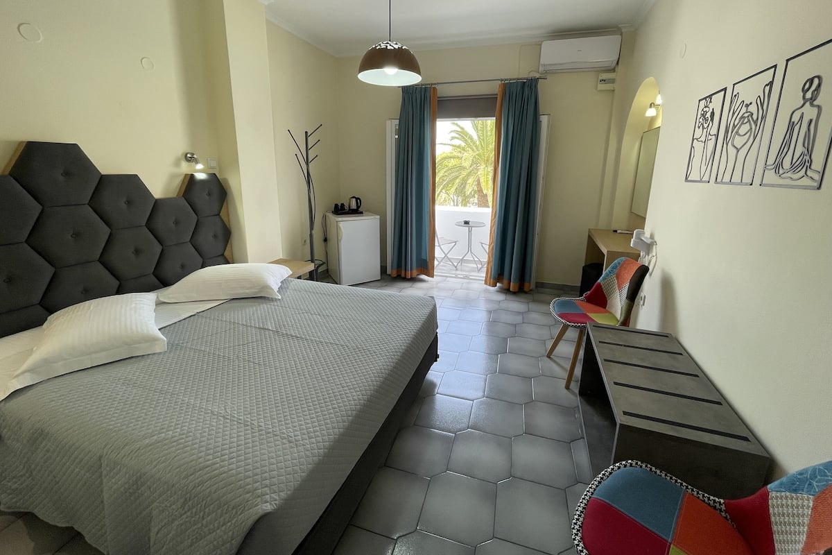 Habitación de hotel con una cama grande, un escritorio pequeño, una silla, una ventana con cortinas y una pared con obras de arte.