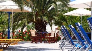 A poolside area with lounge chairs, umbrellas, and a palm tree. - Albatros Hotel (Santorini)