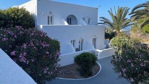 A white building with a curved entrance, surrounded by lush greenery and pink flowers. - Albatros Hotel (Santorini)