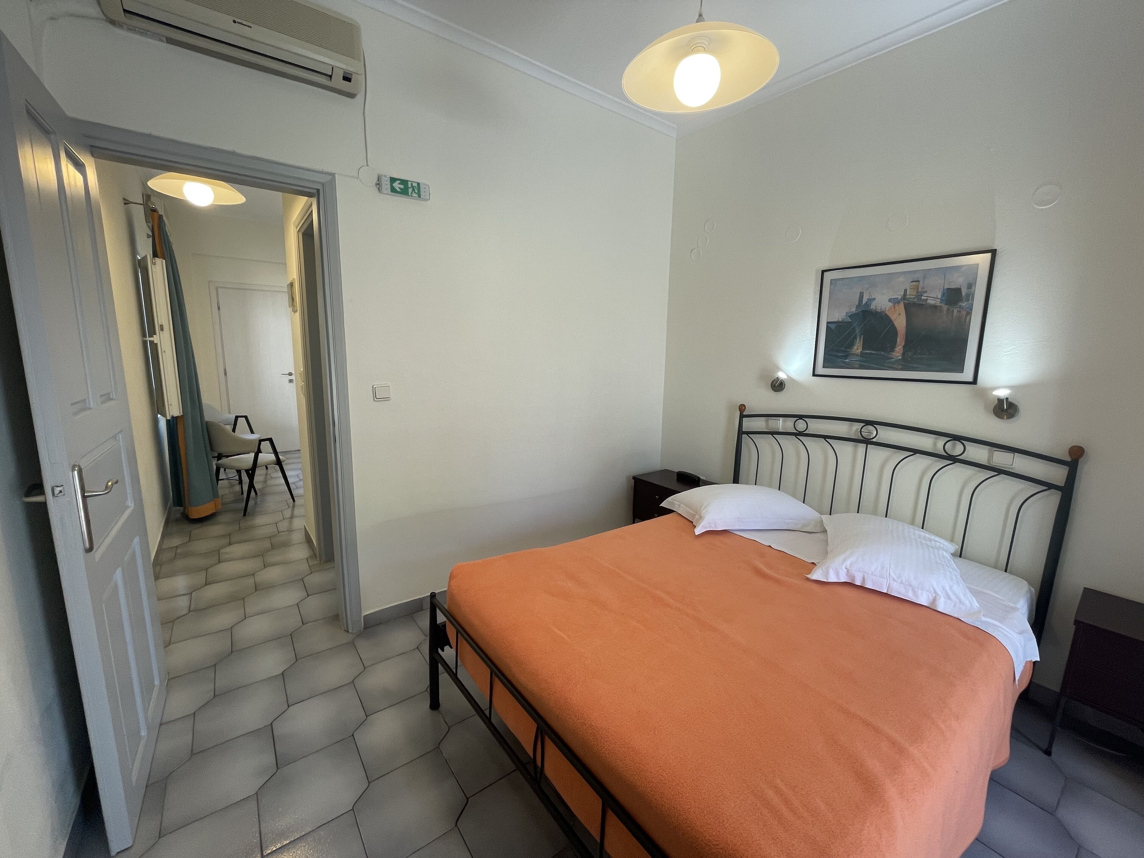 A bedroom with a bed, a nightstand, a painting on the wall, and a door leading to another room.