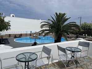 Un espace piscine aménagé sur le toit, avec des chaises longues et des tables, un palmier et un mur en pierre.
