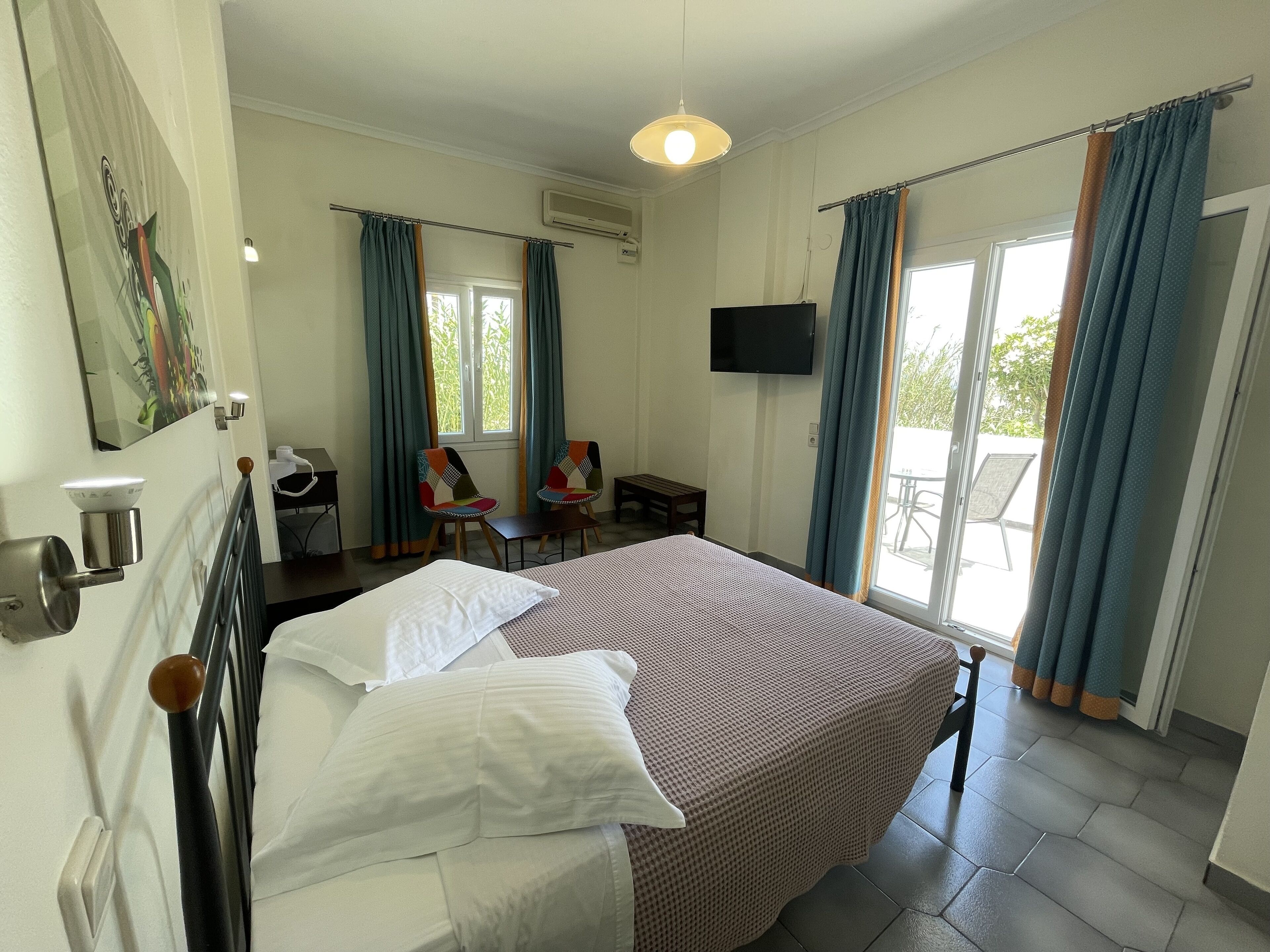 A hotel room with a bed, a desk, two chairs, a TV, and a balcony with curtains.