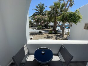 Un balcon avec une table et des chaises bleues, donnant sur un jardin agrémenté de palmiers et de plantes en fleurs.