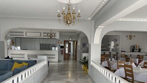 A spacious hotel lobby with a marble floor, a reception desk, a dining area, and a kitchen visible through an archway. - Albatros Hotel (Santorini)
