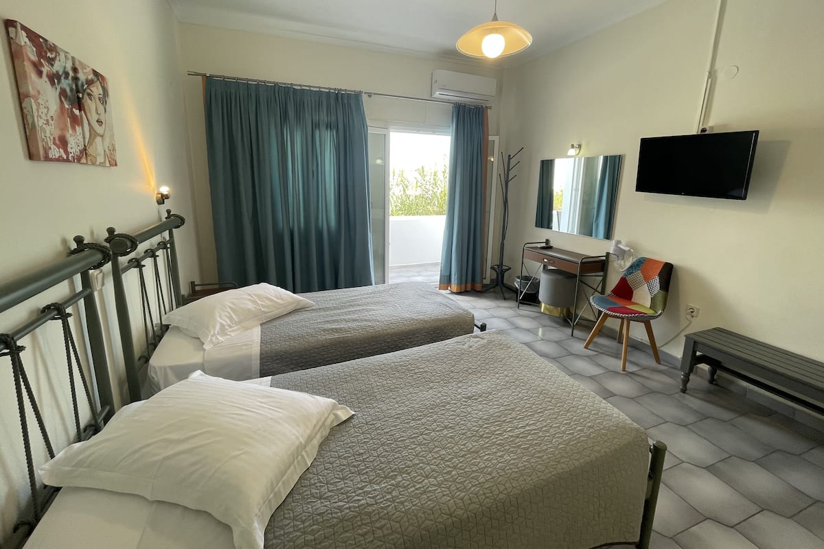 Habitación de hotel con dos camas, un escritorio, una silla, un televisor y un balcón con cortinas.