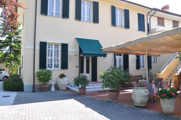 A building with a green awning, potted plants, and a staircase leading to an upper floor. - Verdesolemare (Pietrasanta)