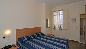 A hotel room with a single bed, a bedside table with a lamp, a remote control, and a window with curtains. - Verdesolemare (Pietrasanta)