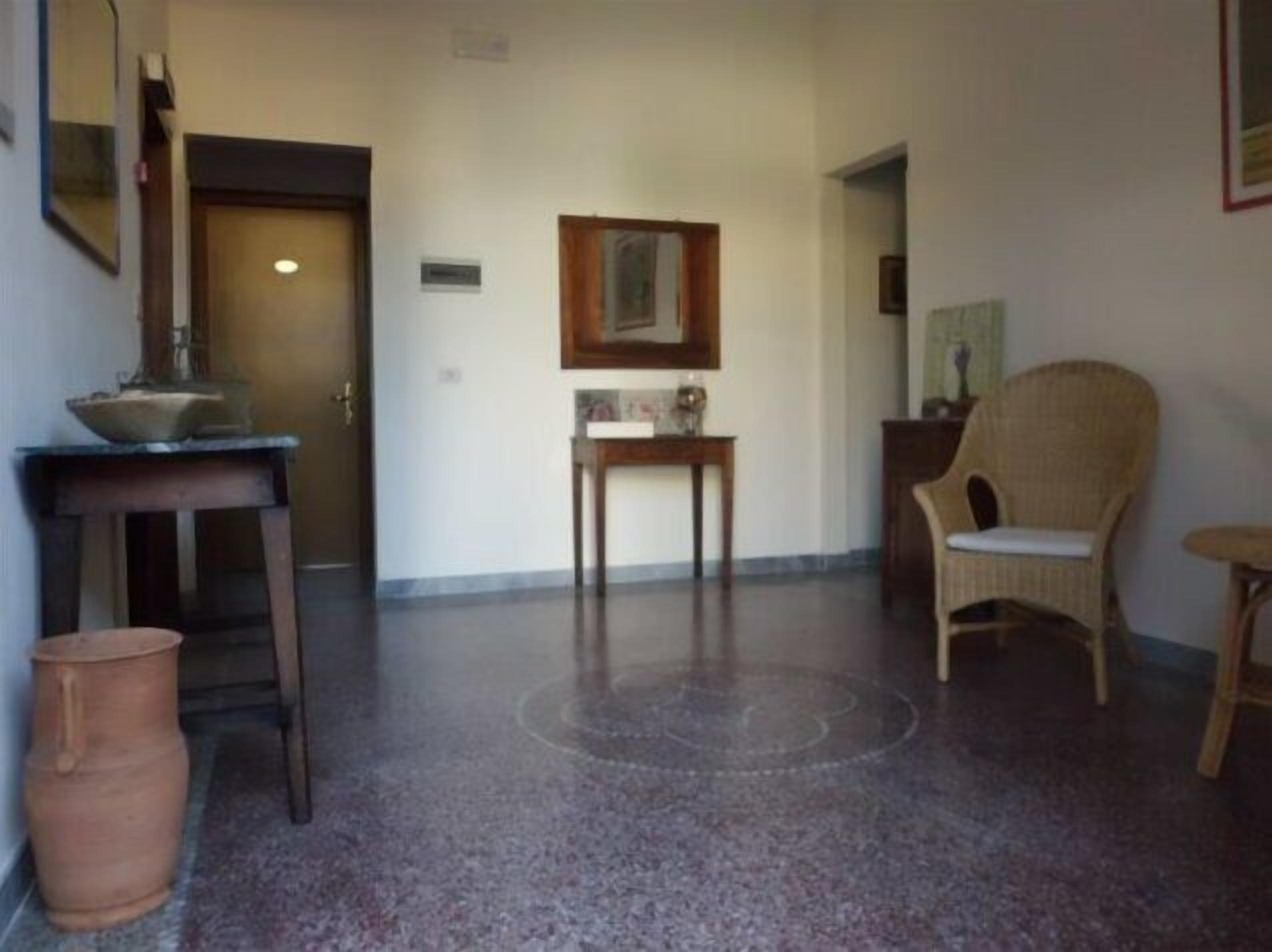 A hallway with a door, a small table with a vase, a wicker chair, and a trash bin.