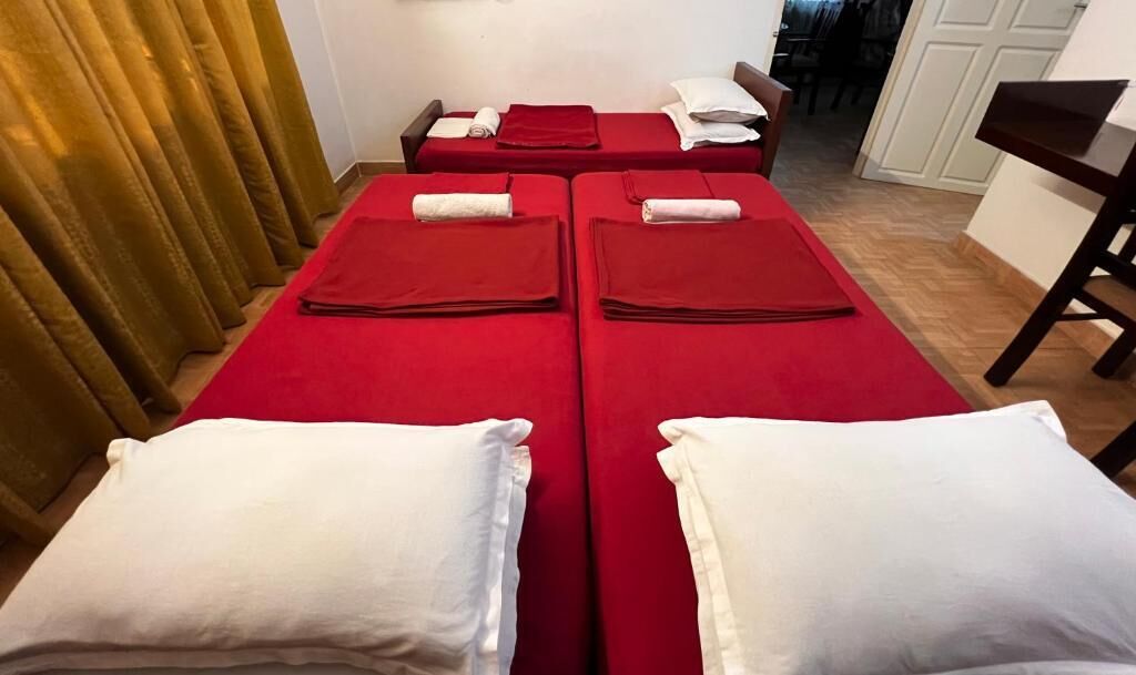 Quarto com duas camas, cada uma com colcha vermelha e almofadas brancas.