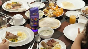 Un bufé de desayuno con diversos platos, como huevos, salchichas y frutas.