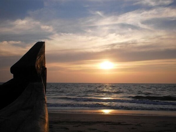 A sunset over the ocean with waves approaching the shore.