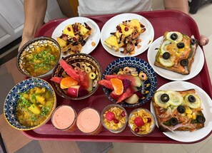 A tray with various food items including a bowl of soup, fruit salad, and slices of pizza. - Reds Residency - Homestay (Kochi)