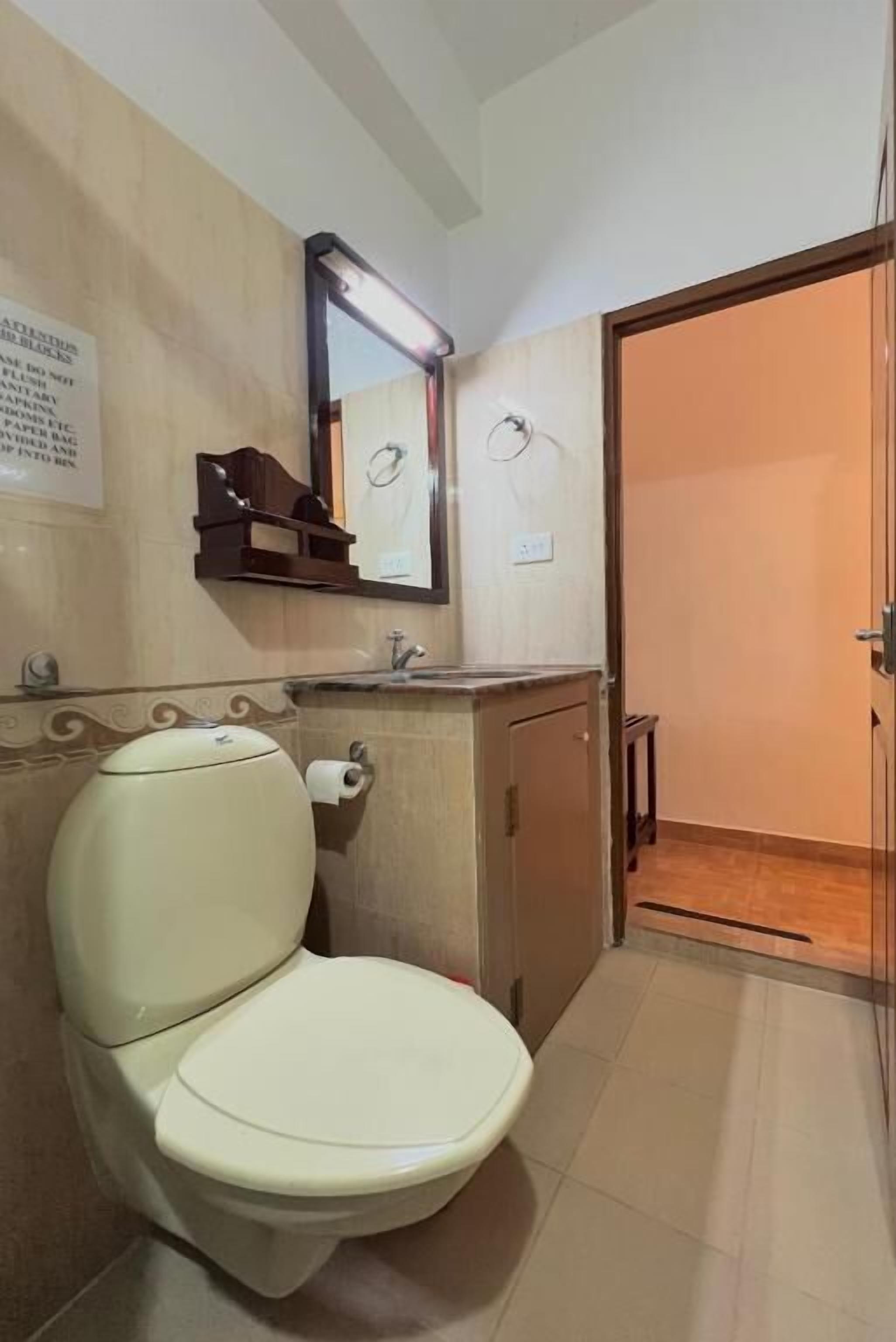 A bathroom with a toilet, sink, mirror, and a door leading to another room.