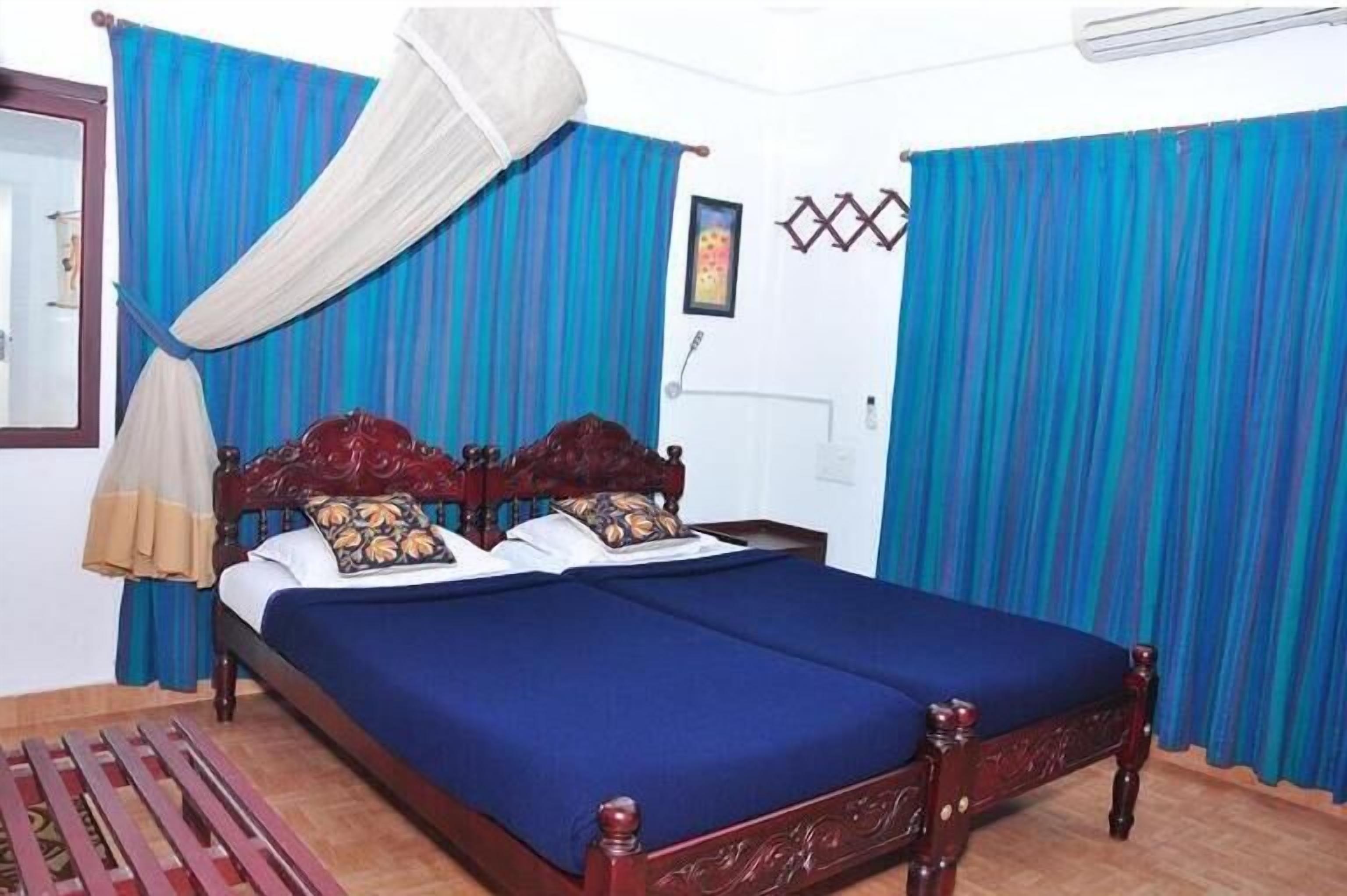 Un lit double avec une couvre-lit bleue et une tête de lit en bois, des rideaux bleus et blancs, et une moustiquaire au-dessus du lit.