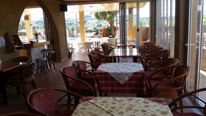 A restaurant with outdoor seating, a view of the hills, and a mix of wooden and wicker chairs. - Summerdays Studios (Rhodes)