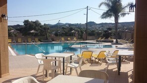 A pool area with lounge chairs and tables, surrounded by palm trees and a view of hills. - Summerdays Studios (Rhodes)