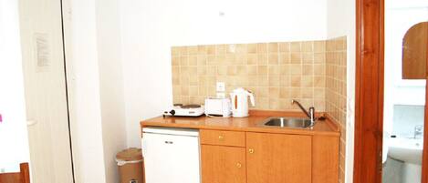 A compact kitchen with wooden cabinets, a white dishwasher, a sink, and a tiled backsplash.