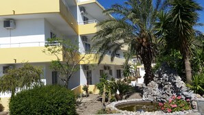 A multi-story building with balconies, a small garden with a pond, and various plants. - Summerdays Studios (Rhodes)