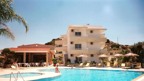 A swimming pool area with lounge chairs and umbrellas, a building with multiple balconies, and a palm tree. - Summerdays Studios (Rhodes)