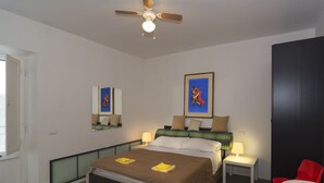 Un dormitorio con cama, mesitas de noche, ventilador de techo y una silla roja.