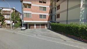 Un edificio residencial de varios pisos con entrada a un garaje, un coche estacionado y cielo despejado.