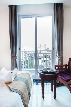 Habitació d'hotel amb llit, una cadira, taula petita i balcó amb vista a la ciutat.