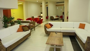 A modern living room with a white sectional sofa, red chairs, a wooden coffee table, and potted plants. - Relax Hotel (Phnom Penh)