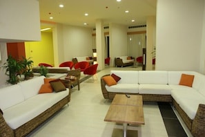 A modern living room with a white sectional sofa, red chairs, a wooden coffee table, and potted plants. - Relax Hotel (Phnom Penh)