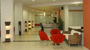 A modern hotel lobby with a reception desk, red chairs, wicker sofas, and a large potted plant. - Relax Hotel (Phnom Penh)