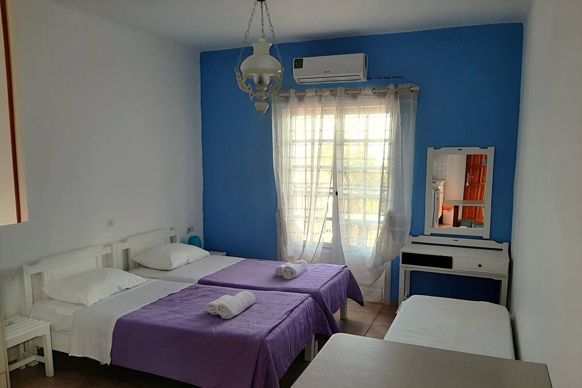 A room with two beds, a table, a mirror, and a window with curtains.