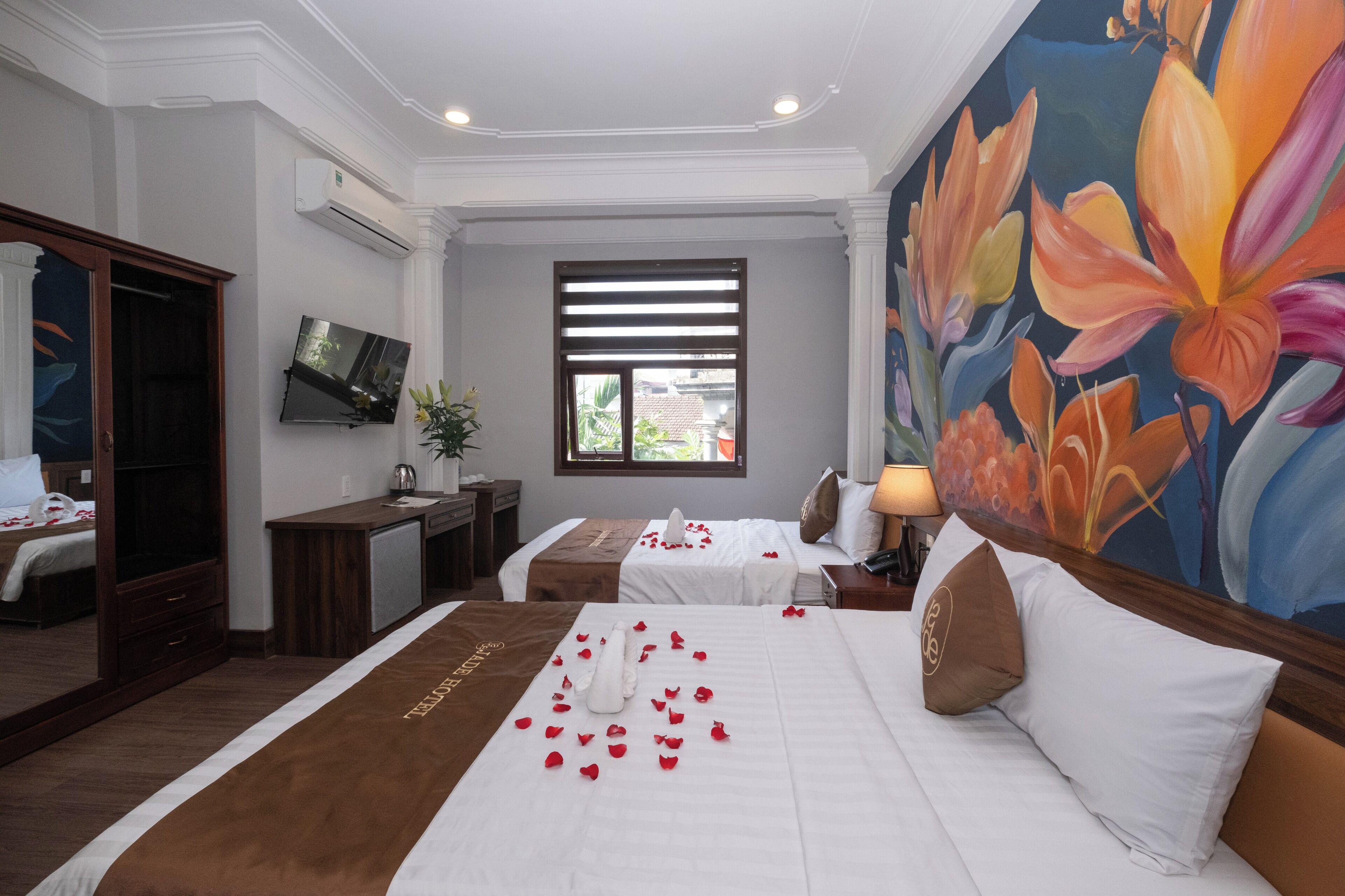Een hotelkamer met twee bedden, een televisie, een schilderij en een raam met zonwering.