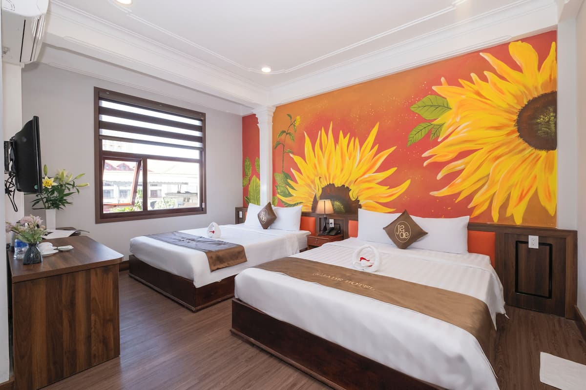 A hotel room with two beds, a wooden desk, a TV, and a large sunflower mural on the wall.