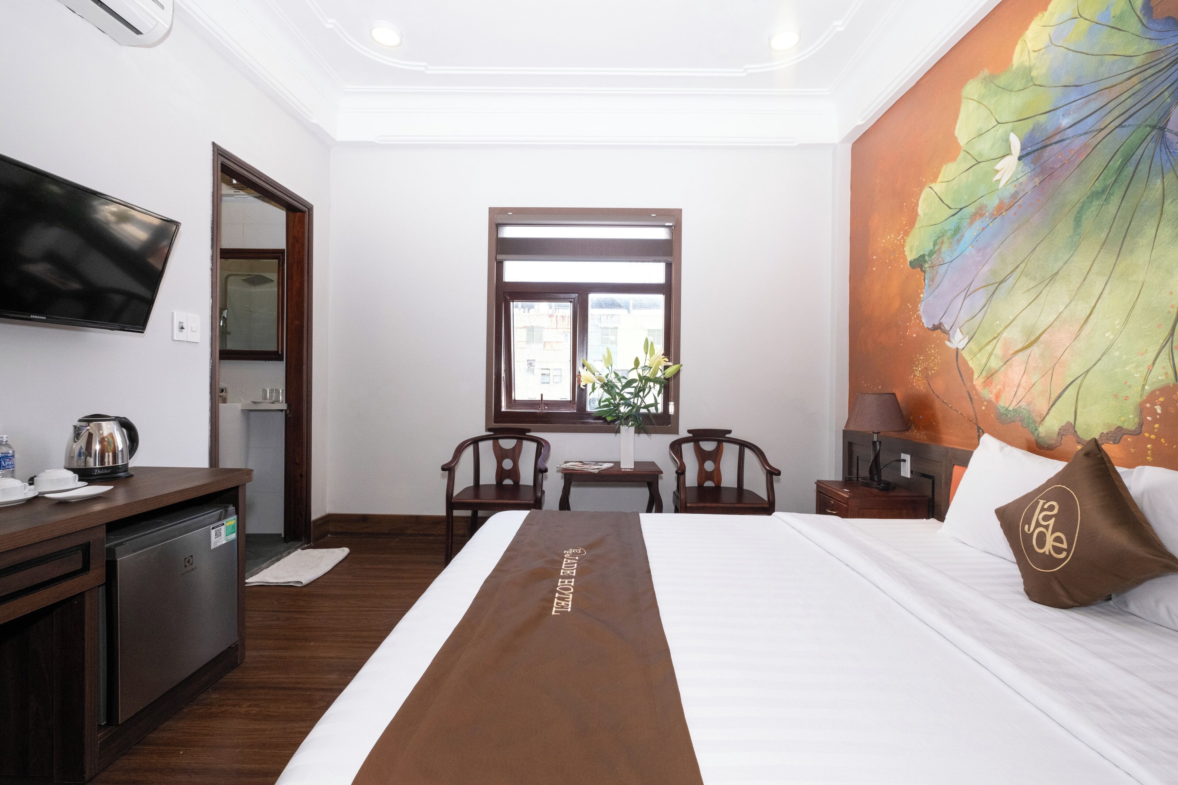 Habitación de hotel con cama, escritorio, televisión, ventana y un cuadro en la pared.