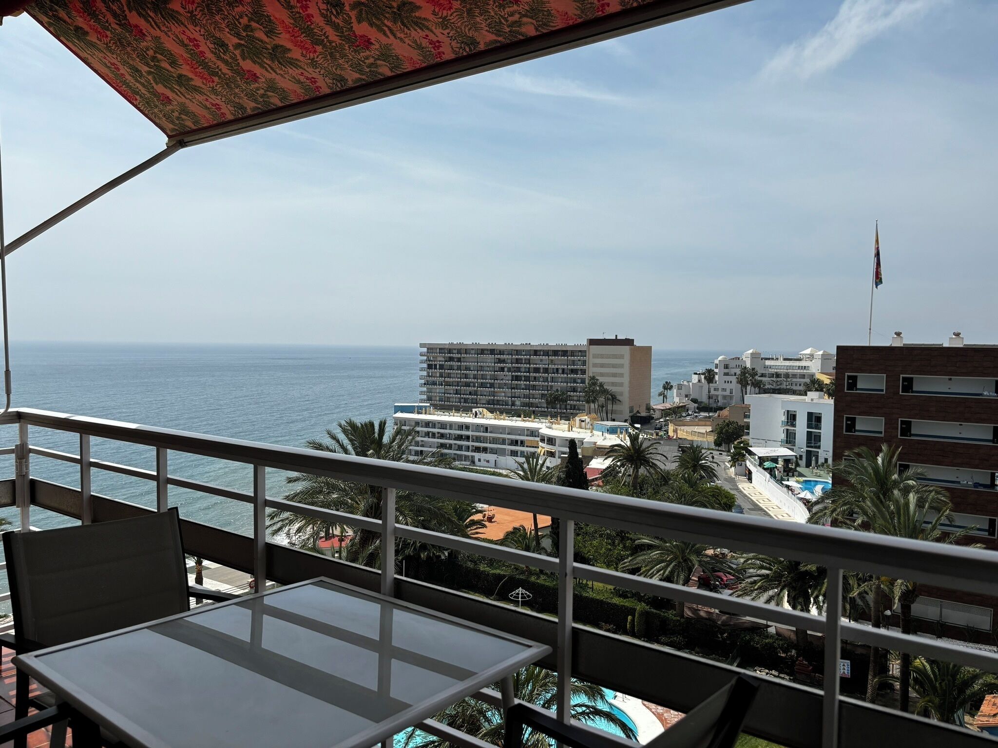 Un balcon avec une table et des chaises, donnant sur une plage et des immeubles.