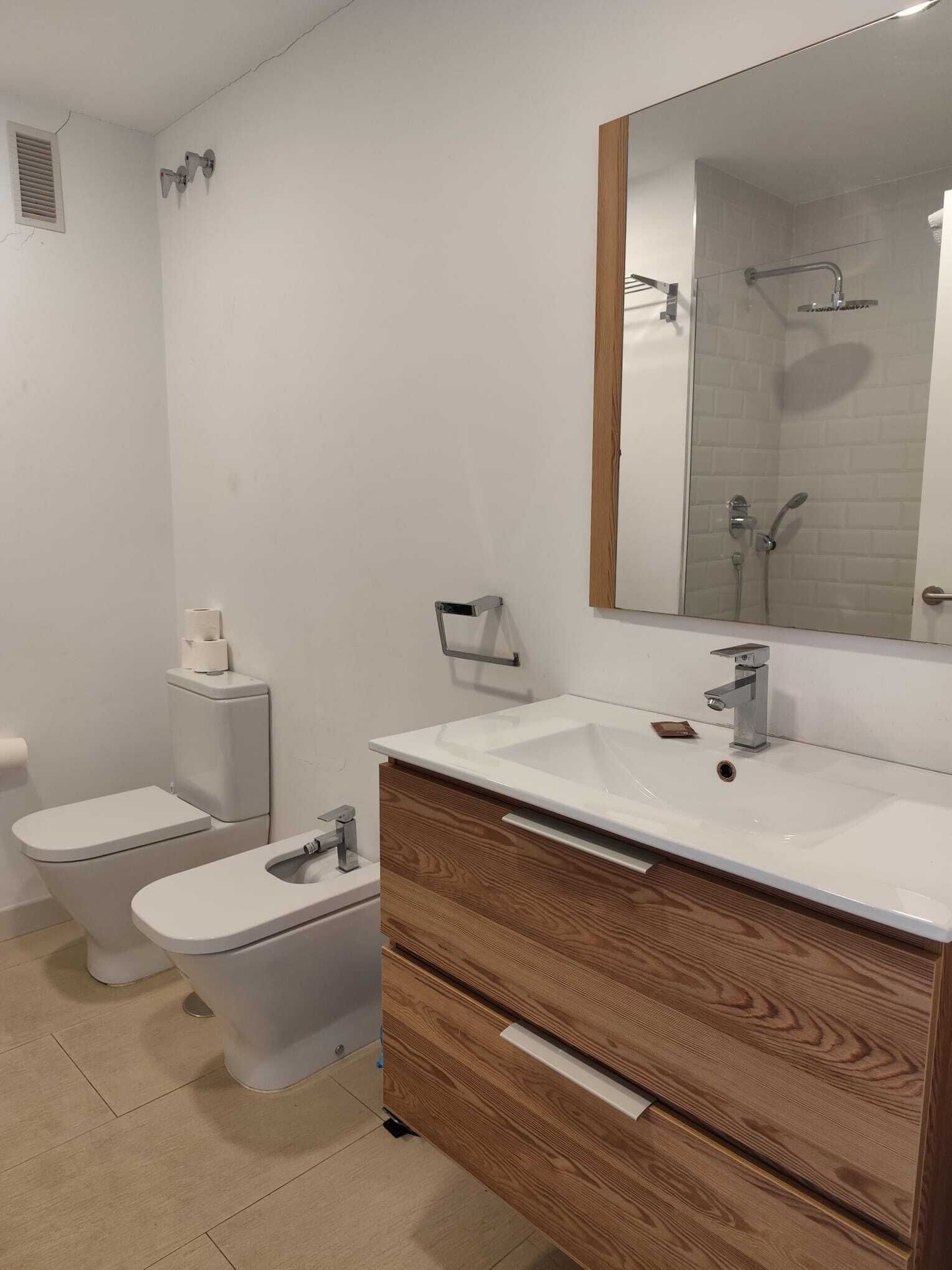 A modern bathroom with a white sink, wooden vanity, two toilets, and a large mirror.