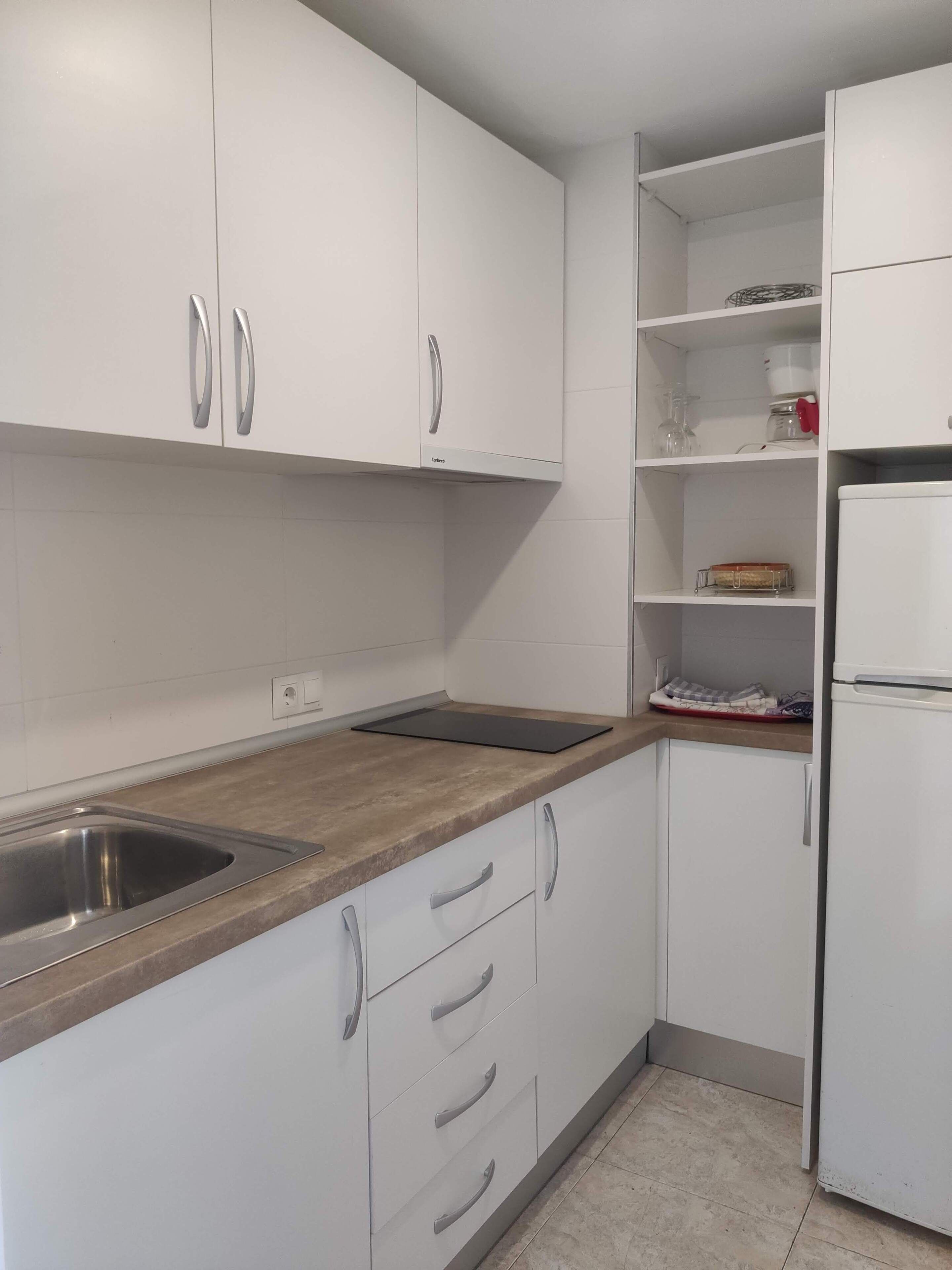 A modern kitchen with white cabinets, a stainless steel sink, and a built-in oven.
