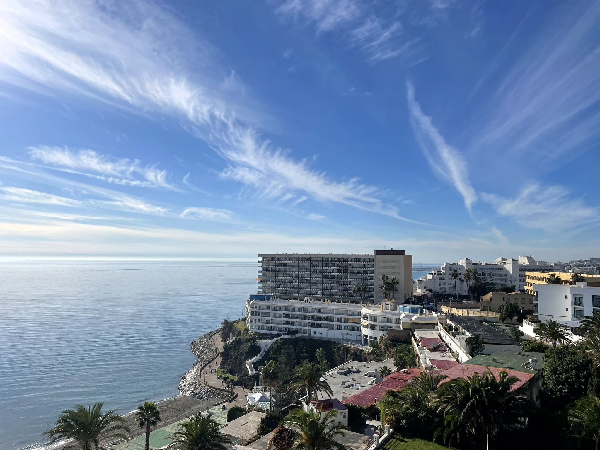 A coastal hotel with multiple floors, a beach, and a view of the sea.