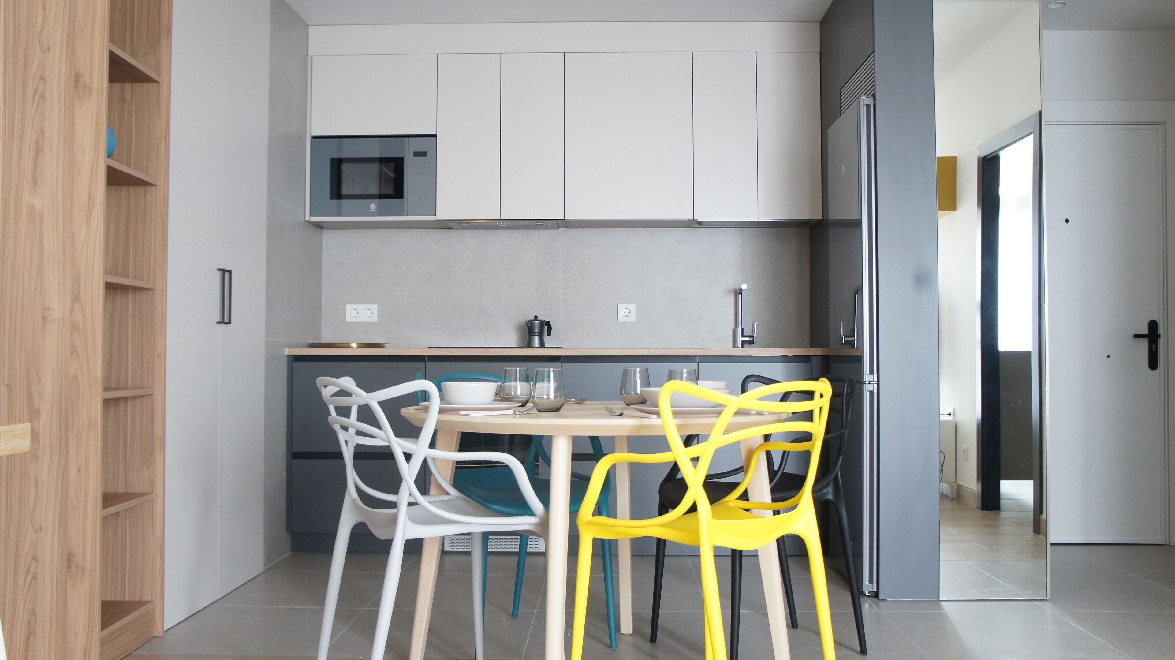 Una cocina moderna con armarios blancos, un microondas y una zona de comedor con mesa y sillas.