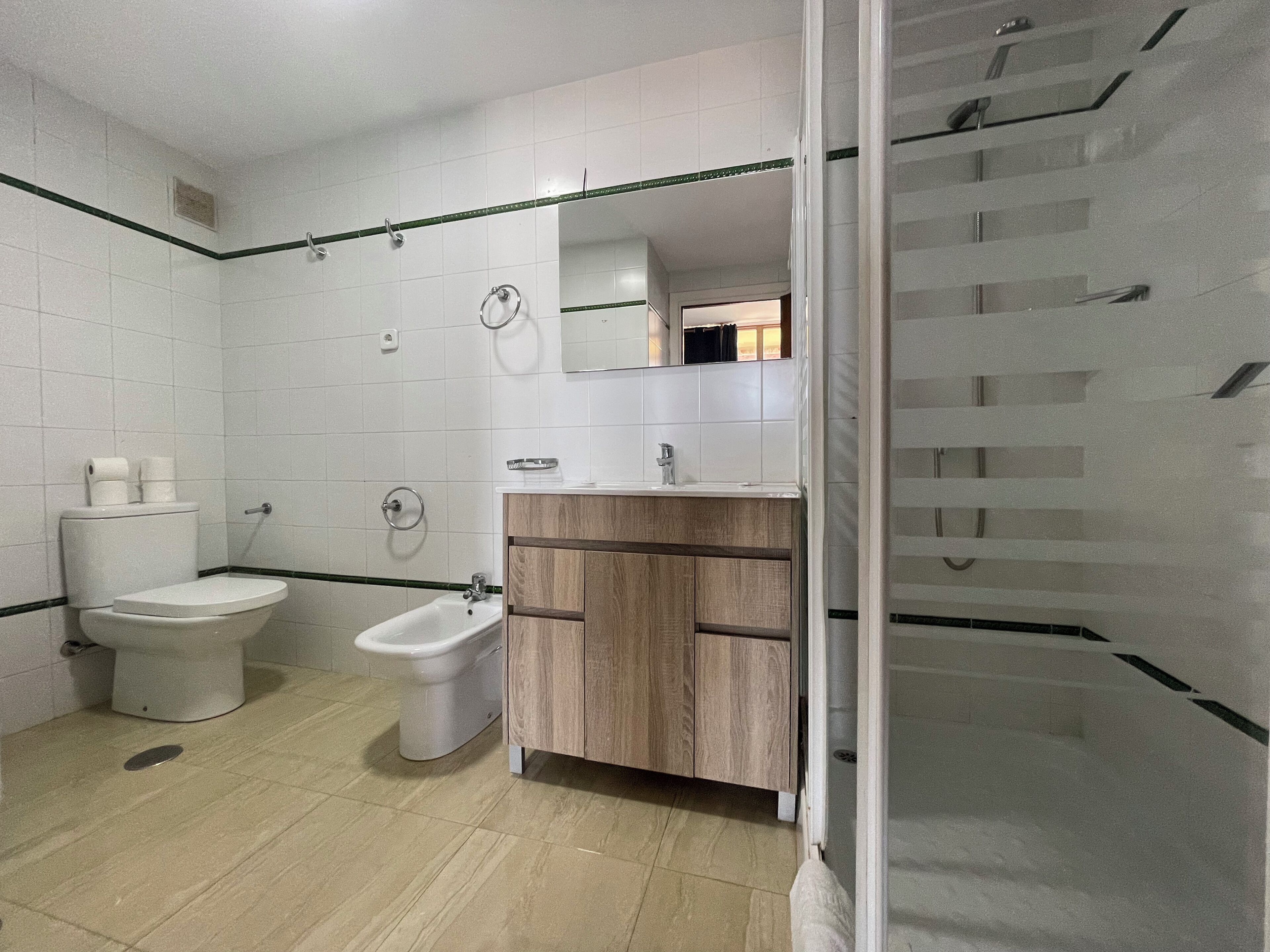 A bathroom with a toilet, bidet, vanity, and a shower area.