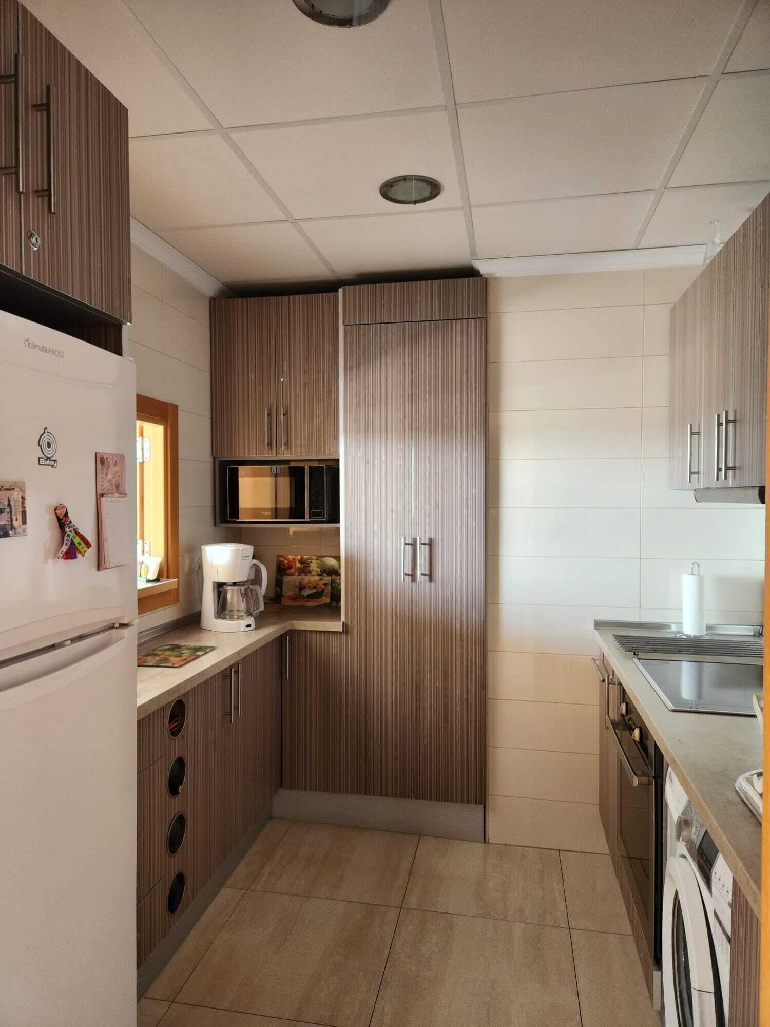 Eine kompakte Küche mit Kühlschrank, Mikrowelle, Kaffeemaschine und Waschmaschine.
