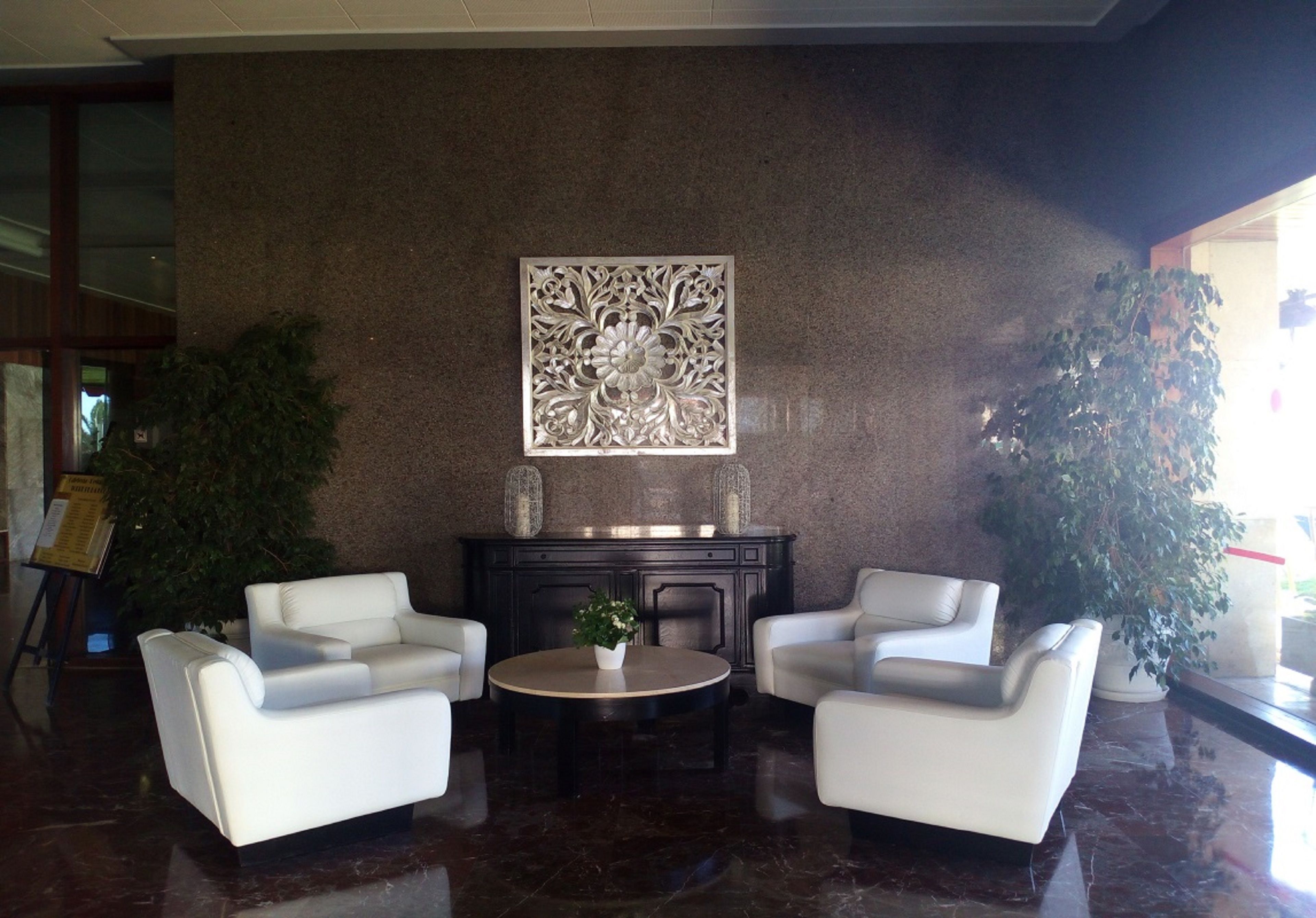 A lobby with two white armchairs, a round table, and a decorative wall piece.